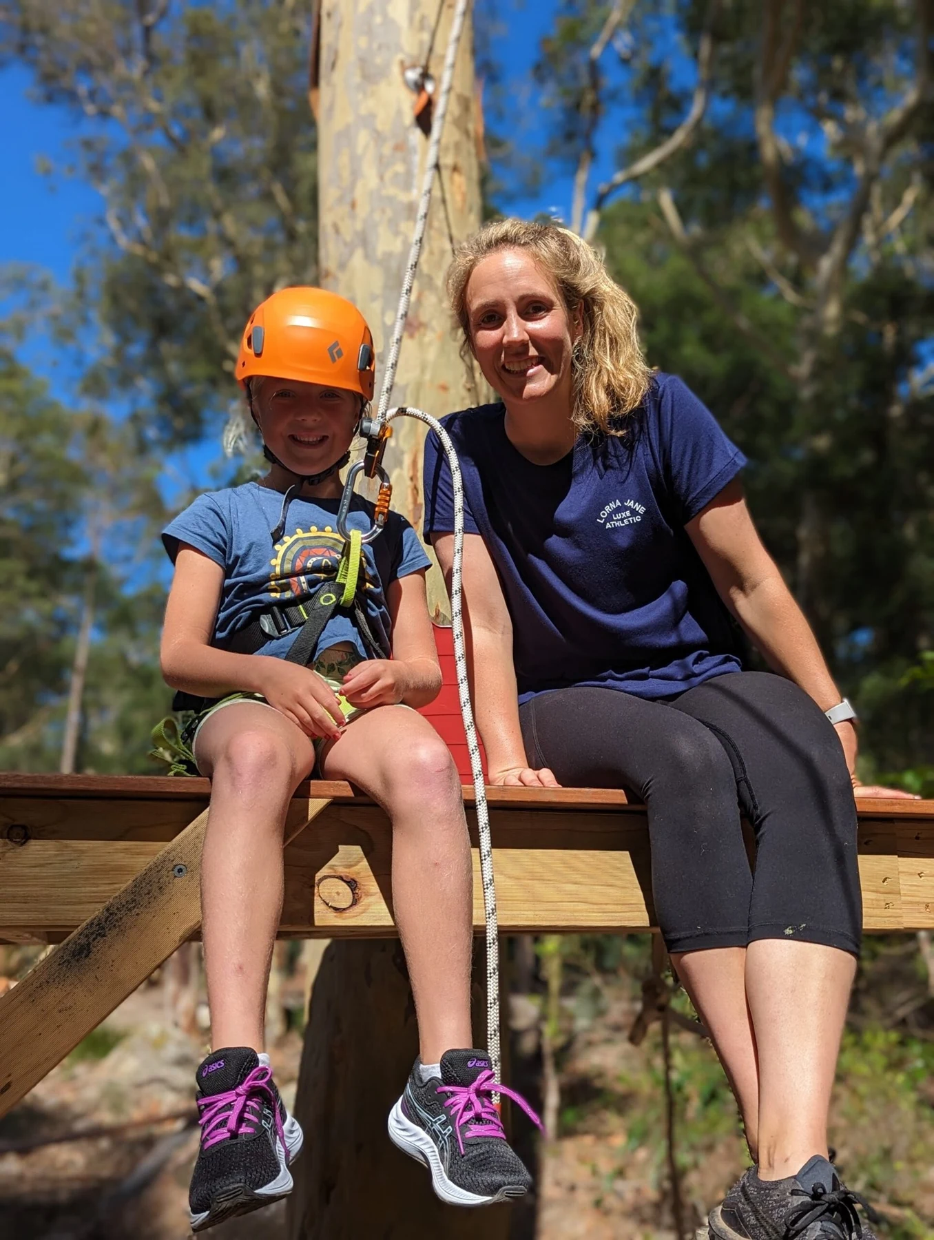An adult and child wearing helmets beside outdoor adventure equipment.